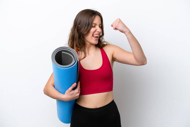 Young sport caucasian woman going to yoga classes while holding a mat isolated on white background celebrating a victory - Photo, image