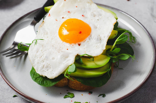 Сэндвич с авокадо с жареным яйцом, здоровый завтрак или закуски на ярком фоне - Фото, изображение