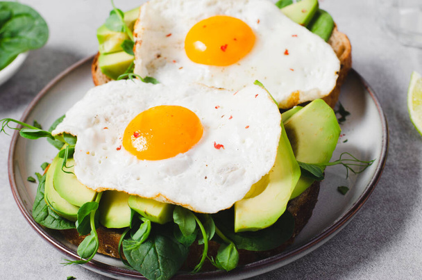 Сэндвич с авокадо с жареным яйцом, здоровый завтрак или закуски на ярком фоне - Фото, изображение