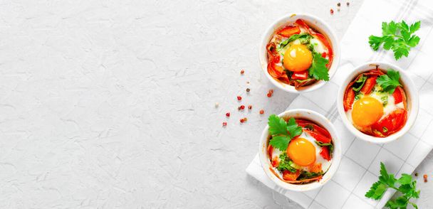Pečená vejce se slaninou, rajčaty, špenátem a bylinkami na jasném pozadí, zdravou snídani nebo svačinku - Fotografie, Obrázek