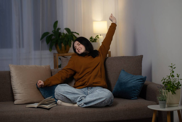 happy teenager girl reading book    on  couch at night - Valokuva, kuva