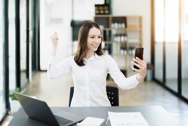 Excited businesswoman using mobile phone while in office - 写真・画像