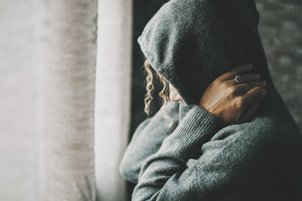 Desperate woman at home indoor wearing sweater with hood on and touching her neck. Stress and life problems for female people alone. Loneliness and depression medical concept. Housewife sad and lonely - Photo, Image