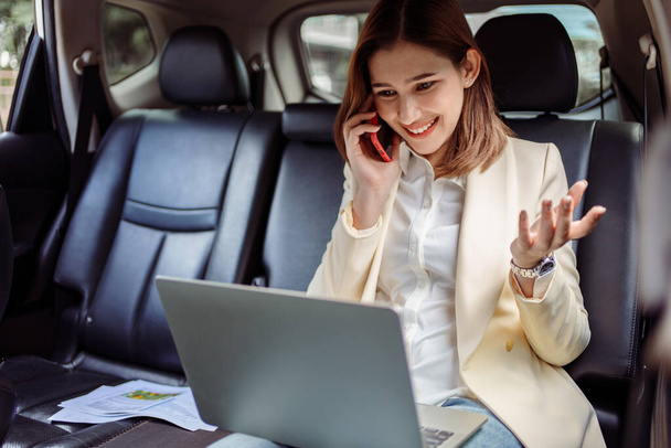 Bizneswoman rozmawia przez telefon komórkowy i używa laptopa w samochodzie. - Zdjęcie, obraz