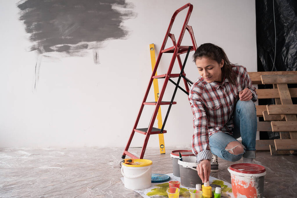 Ev boyama duvarını tamir etmeye çalışan bir kadın yerde boya kutuları ve renk paleti örnekleri seçiyor. Boşluğu kopyala - Fotoğraf, Görsel