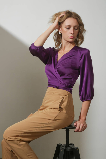 Serie de fotos de estudio de la joven modelo femenina que lleva una blusa de satén de seda violeta y pantalones beige de gran altura - Foto, imagen