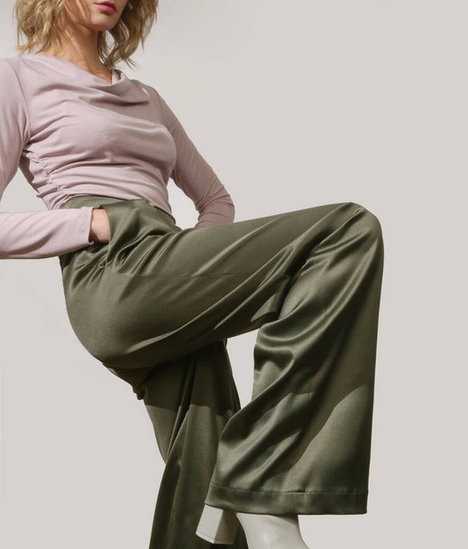 Kobieta modelka ubrana w obcisłą wiskozę z długim rękawem i szerokie zielone satynowe spodnie. Klasyczna, prosta, wygodna, ale stylowa moda. Zdjęcia studyjne. - Zdjęcie, obraz
