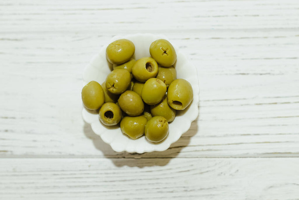 Зелені консервовані оливки в білій мисці на столі
. - Фото, зображення