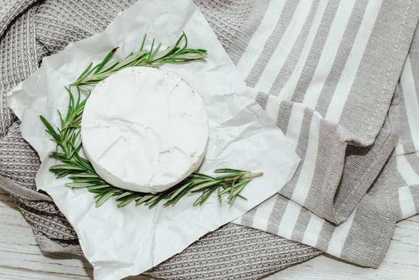 Round cheese in camembert mold with a sprig of rosemary on the table. - Foto, Imagem