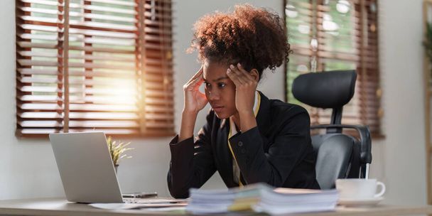 ストレスにさらされたアフリカ系アメリカ人のビジネス女性は、多くの書類書類を扱っています。片頭痛の発作。フリーランス、自宅から仕事. - 写真・画像