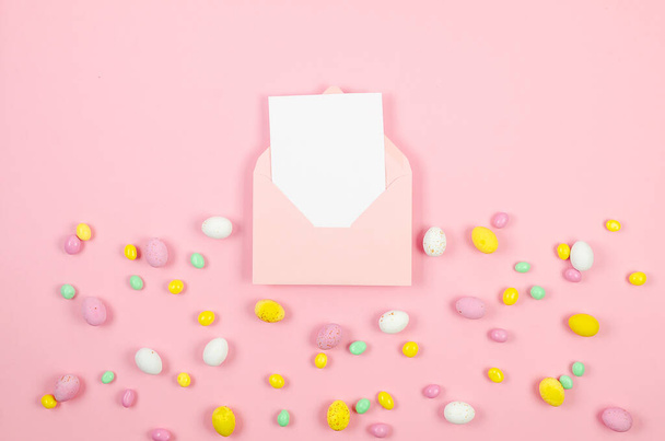 Colorful candy easter eggs on pastel pink background and pink envelope with blank card with place for text. Easter holiday and tradition concept.  - Foto, Imagem