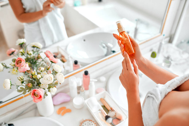 Egy szőke nő egy törülközőben, aki a tükör mosdójában áll, és a reggeli rutinját végzi arc- és bőrápolásra olajjal vagy szérummal. Kozmetológiai és spa eljárások. - Fotó, kép
