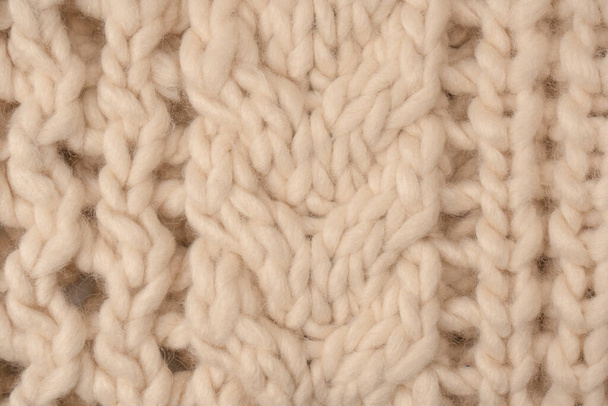 A fragment of beige knitted fabric, knitted from white sheep wool. Knitted background.  - Фото, изображение