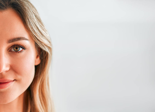 Een close-up portret van een blonde vrouw op de helft van haar gezicht is geïsoleerd tegen een lichte achtergrond. Begrepen, ruimte. Huidverzorging en kosmetologie. - Foto, afbeelding