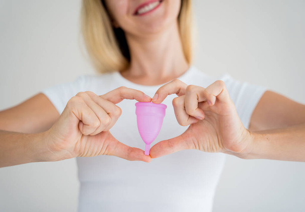 Young beautiful woman at home holding a menstrual cup in her hands. - Valokuva, kuva
