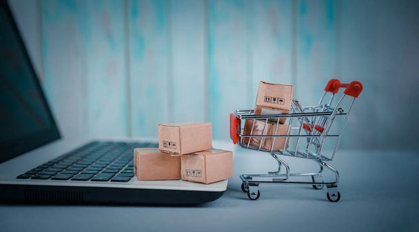 Online shopping, home delivery. Brown paper boxes in a shopping cart with laptop keyboard on table office. Easy shopping with finger tips for consumers. e-commerce and customer experience concept. - Photo, Image