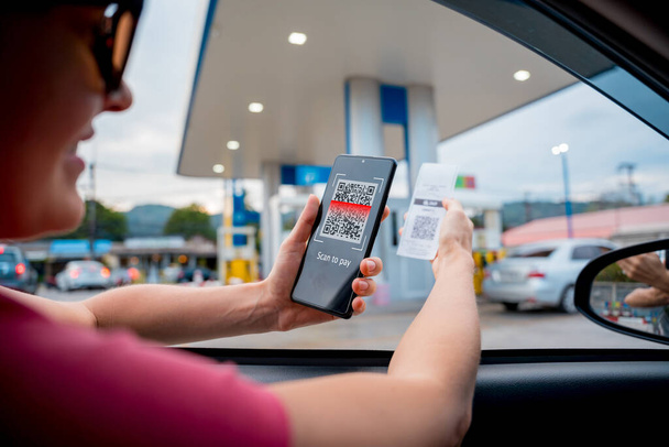 Woman using contactless payment by mobile phone with QR code at car filling station. - Фото, изображение