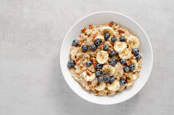 Oatmeal Bowl, Oat Porridge with Blueberry, Banana and Pecans in a Bowl on Bright Grey Background, Healthy Snack or Breakfast - Photo, Image