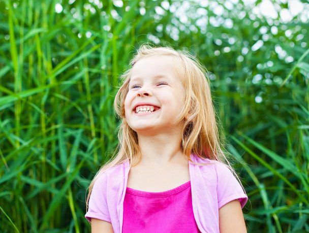 Laughing blonde little girl against canes in summer - Photo, Image