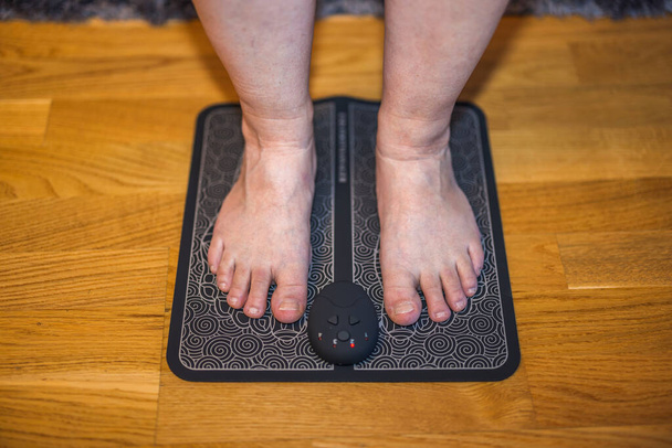 Widok z bliska stóp kobiety na elektrycznym podkładce do masażu stóp. Symulator akupunktury stóp. Szwecja.  - Zdjęcie, obraz