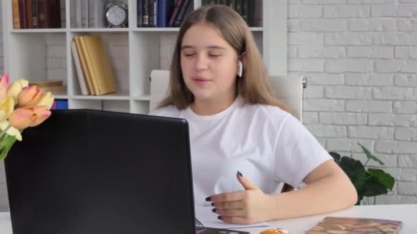 Egy fiatal nő fejhallgatós konferenciát visel, ami laptopbeszélgetésekre hív online tanárokat, tanulnak, otthonról dolgoznak. Női diák és tanulás segítségével számítógépes webkamera chat jegyzetel. Távolsági oktatás 4K - Felvétel, videó