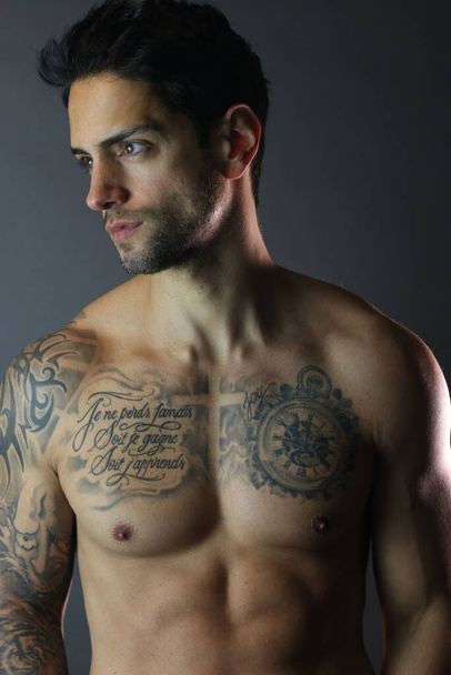 Zeer goed uitziende man met tatoeages poseren shirtloos op grijze achtergrond - Foto, afbeelding