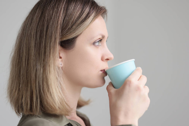 Blondýny žena pije kávu z modrého papírového kelímku drží v ruce v dopoledních hodinách na šedém pozadí. Žena osoba má lahodný nápoj detailní up - Fotografie, Obrázek