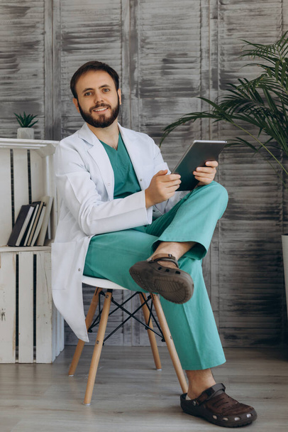 Fejlövés portré mosolygós fiatal férfi háziorvos vagy orvos fehér orvosi egyenruhában és szemüveg néz kamera pózol a kórházban. - Fotó, kép