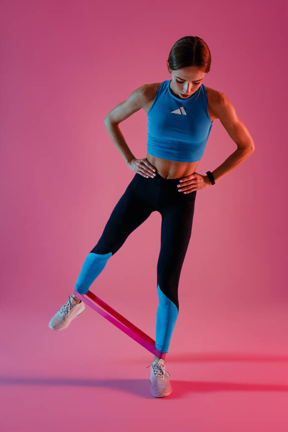 Mujer fitness de pie y estiramiento banda elástica con las piernas en el fondo del estudio. Foto de alta calidad - Foto, imagen