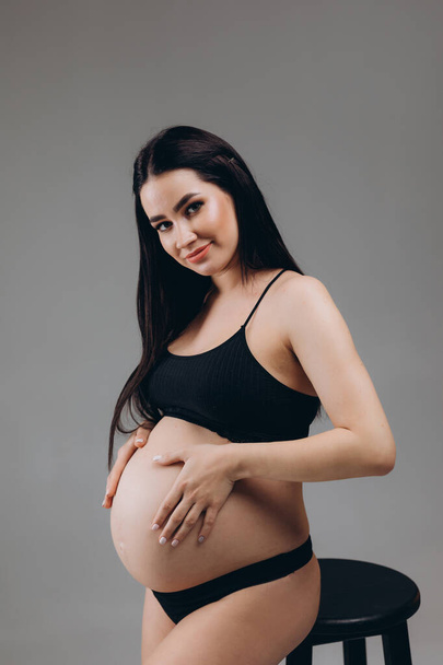 Schwangere berührt ihren Bauch und posiert auf grauem Hintergrund - Foto, Bild