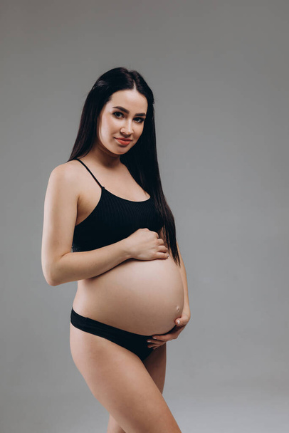 Portrait Of Happy Pregnant Woman In Lingerie With Smile Face Made Of Cream On Her Belly Posing Over Beige Background, Beautiful Young Expectant Female In Underwear Smiling At Camera - Foto, Bild