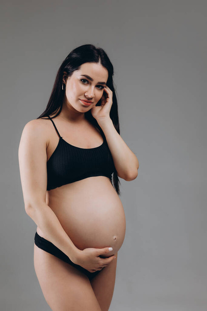 Portrait Of Happy Pregnant Woman In Lingerie With Smile Face Made Of Cream On Her Belly Posing Over Beige Background, Beautiful Young Expectant Female In Underwear Smiling At Camera - Photo, Image