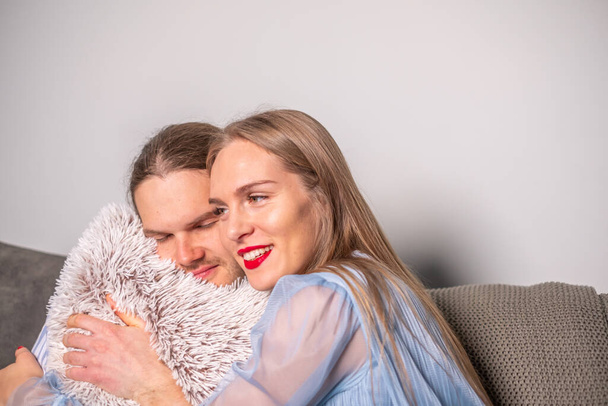 Das junge verliebte lächelnde Paar streichelt ein flauschiges hellgraues Kissen. Die Freude am Zusammensein. - Foto, Bild