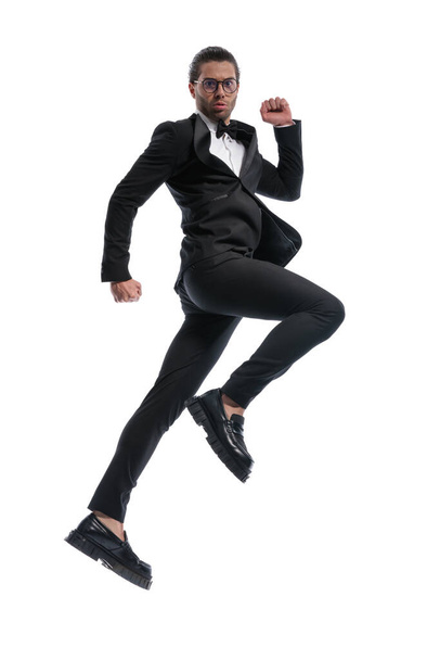 attractive businessman jumping high into the sky and wearing glasses against white studio background - Фото, зображення