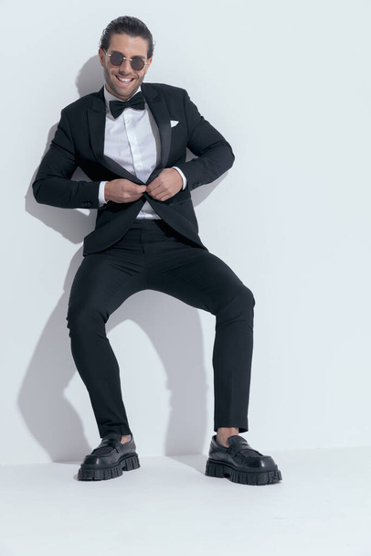 handsome businessman opening his tuxedo and laughing with joy, wearing glasses against white studio background - Fotografie, Obrázek