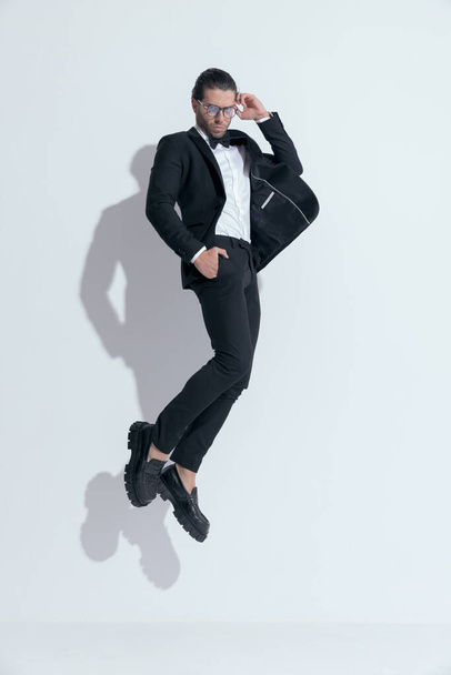 sexy businessman jumping with hands in pockets and fixing glasses, wearing glasses against white studio background - Fotoğraf, Görsel