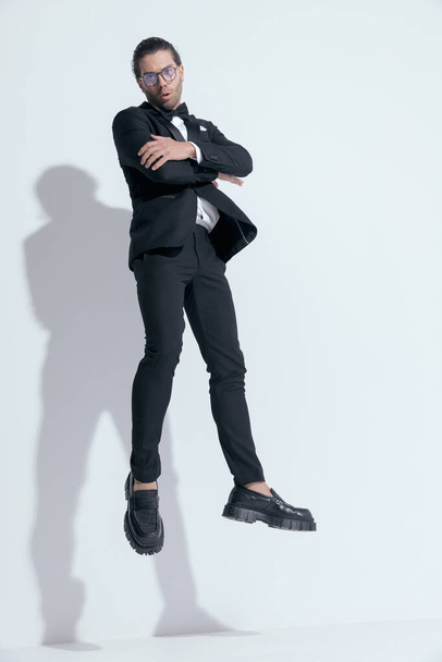 joven hombre de negocios saltando y cruzando los brazos, con gafas sobre fondo blanco estudio - Foto, Imagen