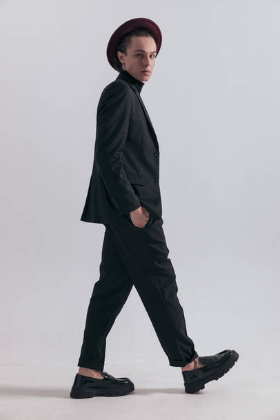 Photo de mode d'un bel homme d'affaires marchant sur le côté et regardant la caméra et portant une tenue élégante sur fond de studio gris - Photo, image