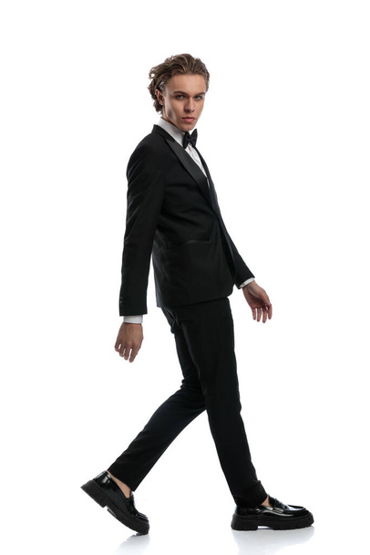 elegant businessman walking to side and looking at camera, wearing a formal outfit against white studio background - Photo, Image