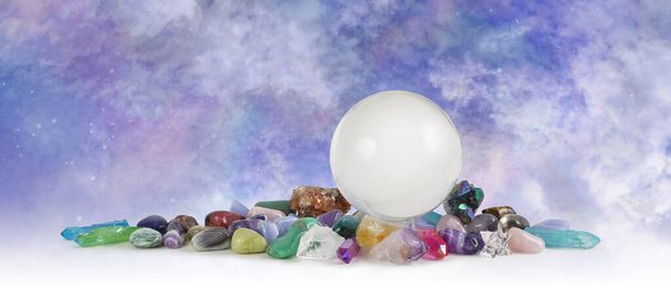 Large clear crystal ball celestial crystal healing banner - skrying sphere sitting atop selection of tumbled healing stones in front of heavenly sky background with copy space  - Photo, Image
