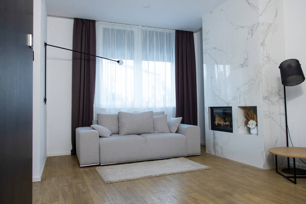 Cozy sofa with the gray cushions located by a large window in the living room - Foto, Bild