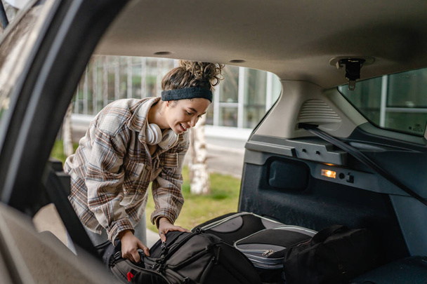 One young beautiful woman student travel concept female take luggage baggage suitcase and other stuff and belongings from the back of her car while moving into dormitory on college campus real people - Fotó, kép
