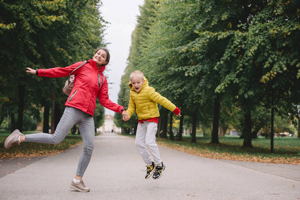 Mother and son jumping in the autumn park. Fall Season. Happy young beautiful mother and her son have a walk in the park - Fotografie, Obrázek