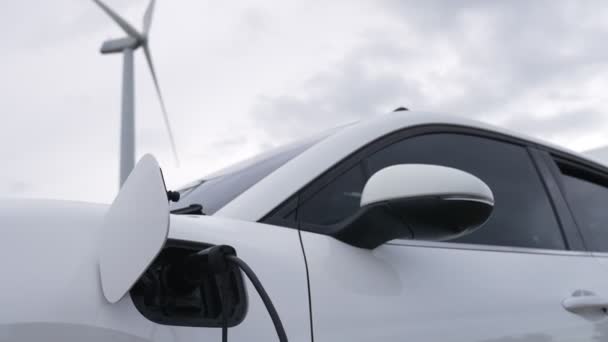 Progressive future energy infrastructure concept of electric vehicle being charged at charging station powered by green and renewable energy from a wind turbine in order to preserve the environment. - Footage, Video