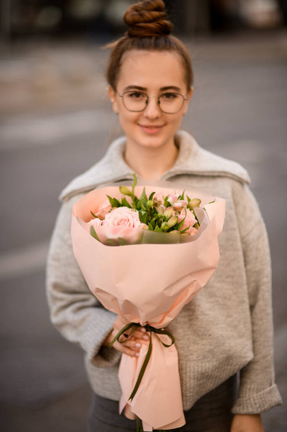 beautiful bouquet of pink roses in wrapping paper in the hand of a young attractive woman - 写真・画像