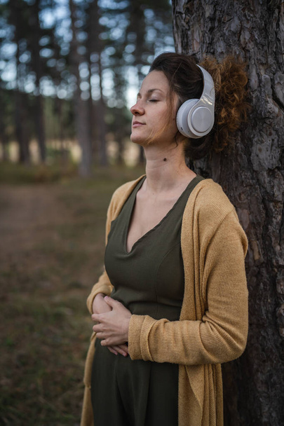 Одна жінка молода доросла біла жінка стоїть на самоті в парку або в лісі на природі з навушниками, які готуються до керованої медитації самодопомоги, практикують концепцію емоційного балансу
 - Фото, зображення