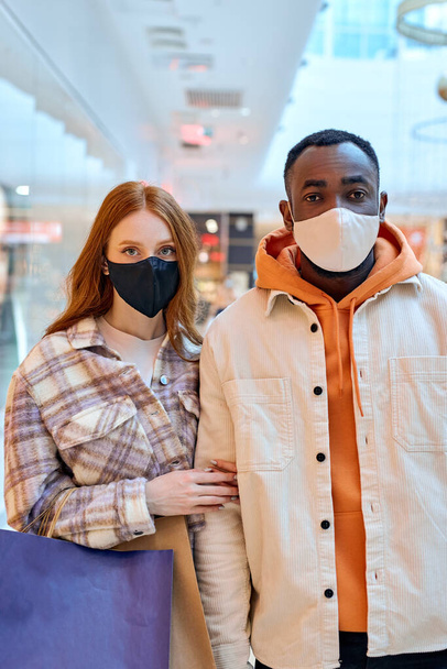 serious diverse couple standing at mall, looking at camera, health care, wellness, protection from serious illness - Fotografie, Obrázek