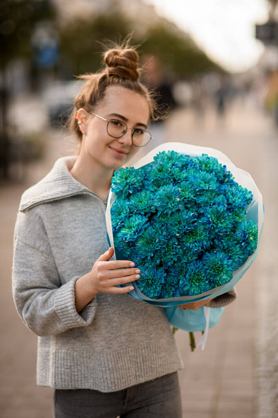 mujer joven sonriente con gran ramo hermoso de crisantemos azules en papel de envolver en la mano - Foto, imagen