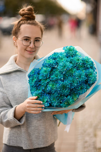 happy young woman with large beautiful bouquet of blue chrysanthemums in wrapping paper in her hand - Fotoğraf, Görsel