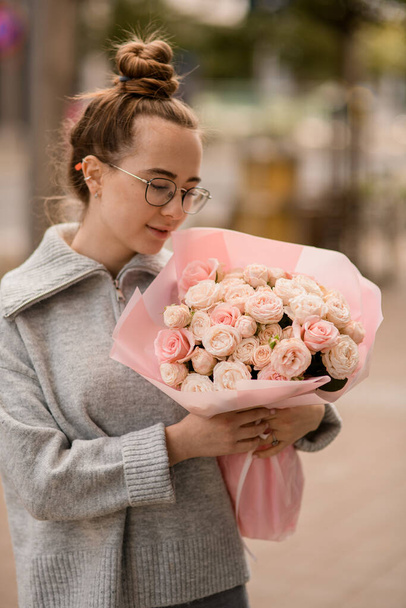 charming view of young handsome young woman with lush luxury bouquet of pink roses in wrapping paper in the hand - Fotó, kép
